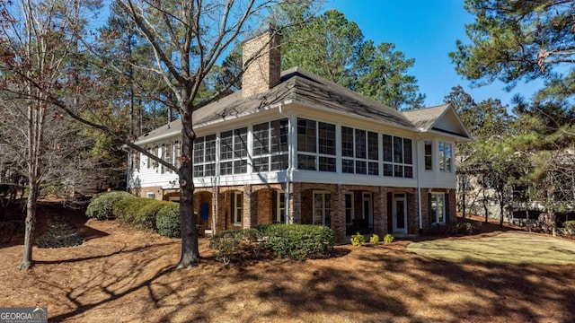 rear view of property with brick siding, a chimney, and a sunroom