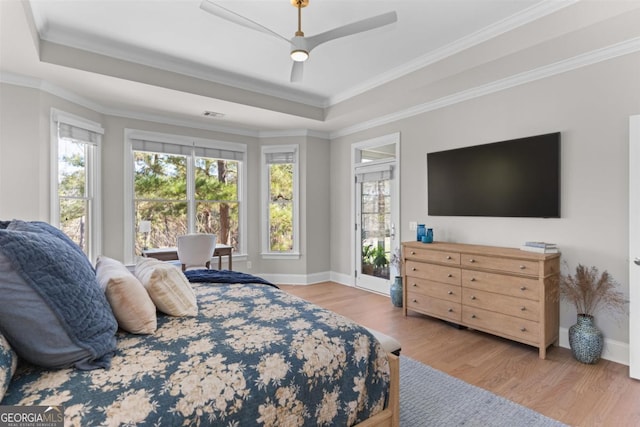 bedroom featuring crown molding, a tray ceiling, wood finished floors, and baseboards