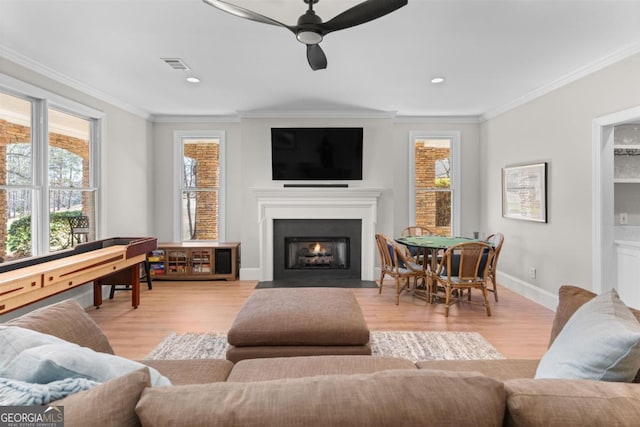 living room featuring light wood-type flooring, a fireplace with flush hearth, visible vents, and crown molding