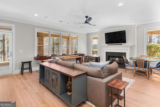 living area with ornamental molding, light wood finished floors, a glass covered fireplace, and visible vents