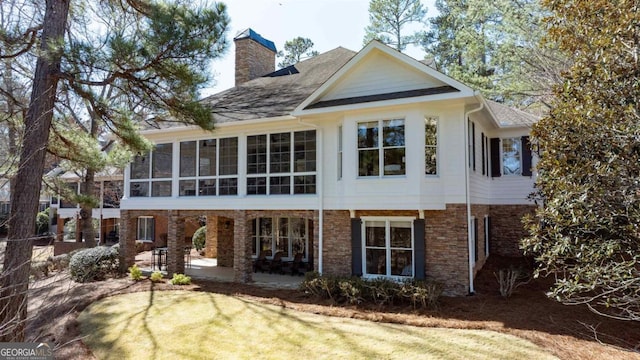 back of house with brick siding, a chimney, a sunroom, and a patio