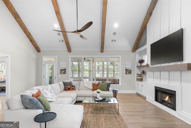 living area featuring vaulted ceiling with beams, a warm lit fireplace, light wood-style floors, and a wealth of natural light