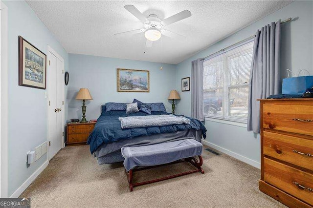 bedroom with visible vents, baseboards, light colored carpet, ceiling fan, and a textured ceiling