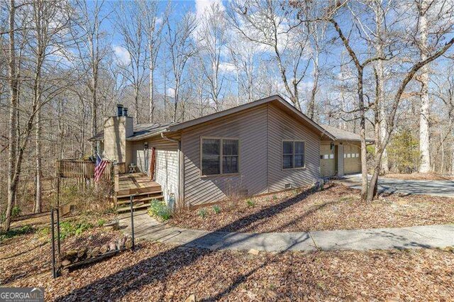 view of property exterior with a deck, concrete driveway, a chimney, and an attached garage