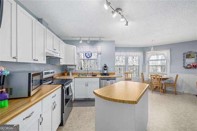 kitchen with appliances with stainless steel finishes, white cabinets, a sink, and under cabinet range hood