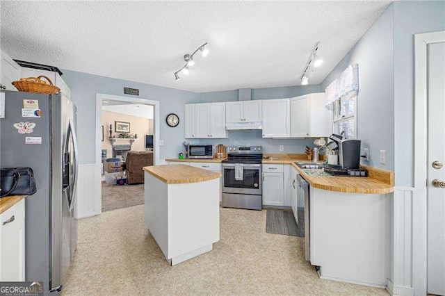 kitchen featuring stainless steel appliances, white cabinetry, wooden counters, and under cabinet range hood