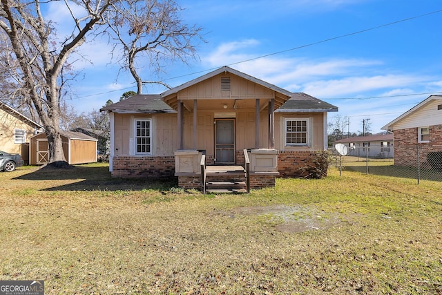 bungalow with an outbuilding, fence, a shed, a front lawn, and brick siding