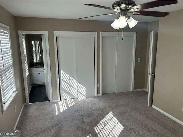 unfurnished bedroom featuring carpet, multiple windows, baseboards, and two closets