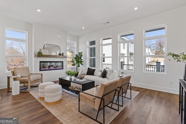 living room featuring recessed lighting, dark wood-type flooring, and a glass covered fireplace