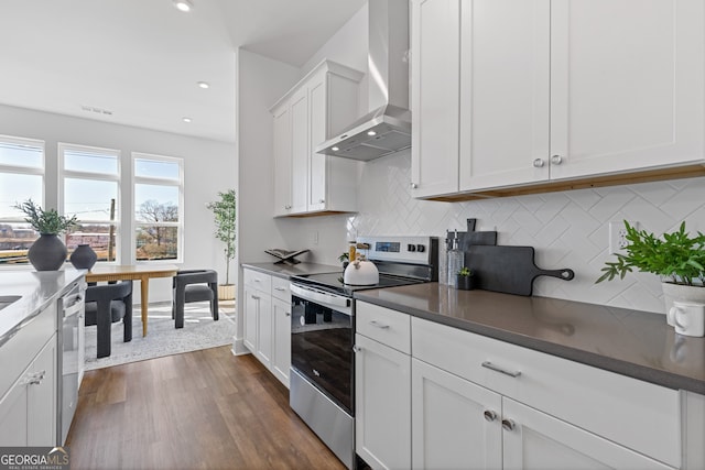 kitchen with white cabinets, dark countertops, dark wood-style flooring, stainless steel appliances, and wall chimney range hood