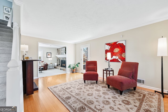 living area with light wood finished floors, visible vents, ornamental molding, a stone fireplace, and baseboards