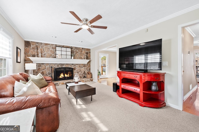 living room with baseboards, a ceiling fan, ornamental molding, carpet, and a stone fireplace