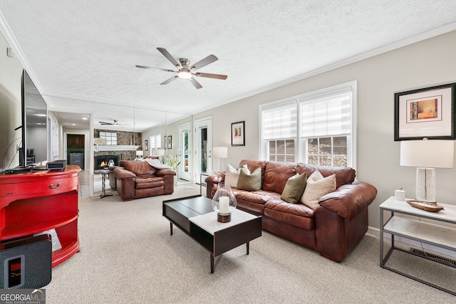 living room with a ceiling fan, crown molding, a stone fireplace, and a textured ceiling