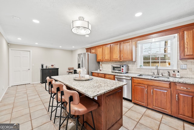 kitchen featuring stainless steel appliances, backsplash, brown cabinetry, a sink, and a kitchen bar