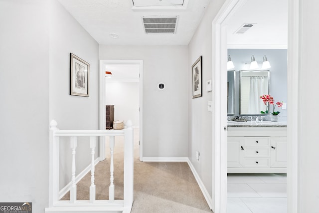 hall featuring light carpet, a sink, visible vents, and baseboards