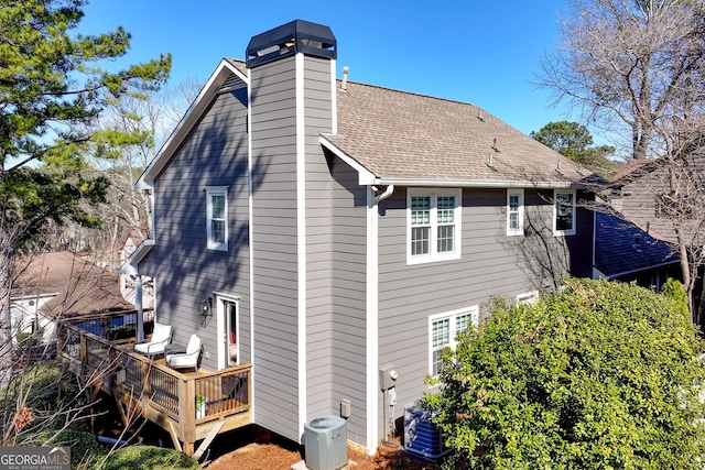 back of house featuring roof with shingles, a chimney, central AC unit, and a wooden deck