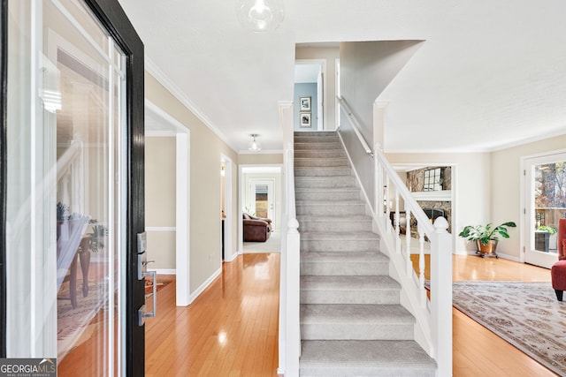 stairway with baseboards, a stone fireplace, wood finished floors, and crown molding