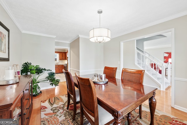 dining space featuring crown molding, a notable chandelier, light wood-style flooring, and stairs