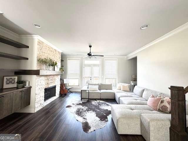 living area featuring ceiling fan, ornamental molding, dark wood finished floors, and a stone fireplace