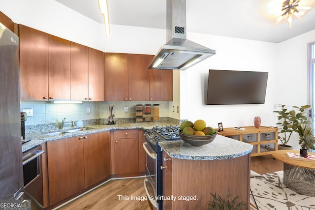 kitchen featuring island exhaust hood, a sink, light wood-style floors, appliances with stainless steel finishes, and a peninsula