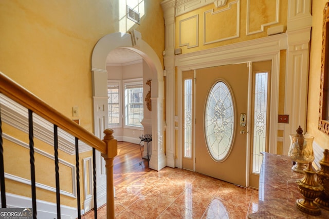 entrance foyer with arched walkways, visible vents, ornamental molding, baseboards, and stairs