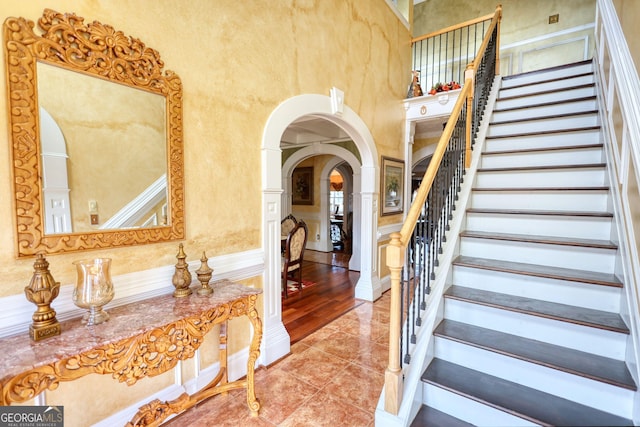 stairway featuring a towering ceiling, tile patterned flooring, and arched walkways