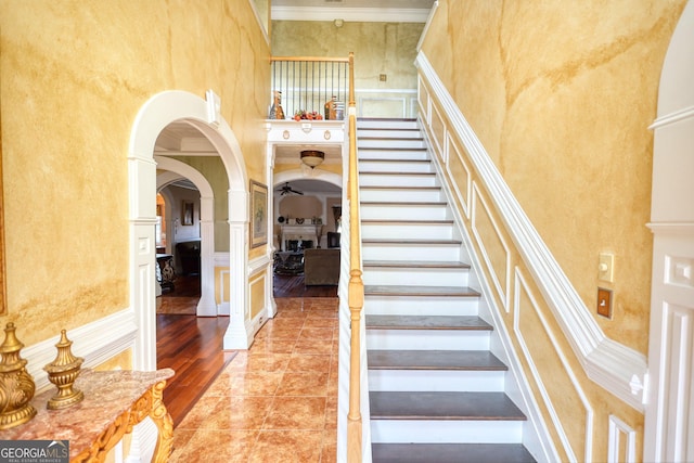 stairway featuring arched walkways, a ceiling fan, ornamental molding, wood finished floors, and a high ceiling