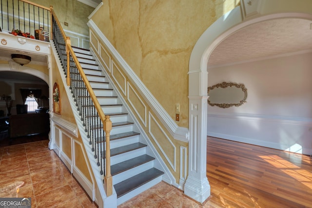 stairway with arched walkways, crown molding, a textured ceiling, and wood finished floors