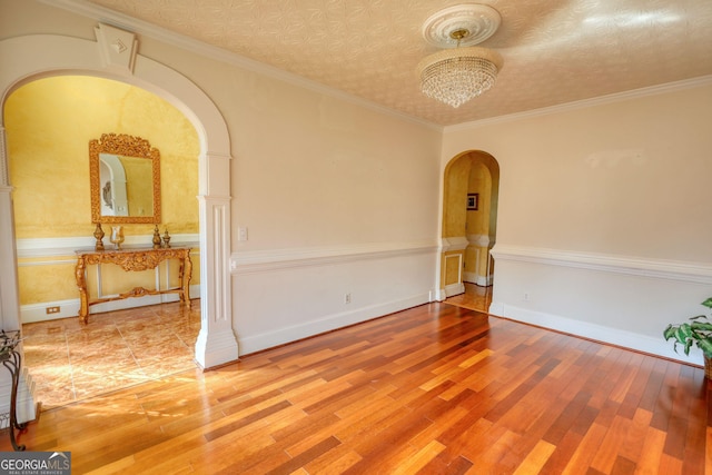 spare room featuring arched walkways, ornamental molding, and wood finished floors