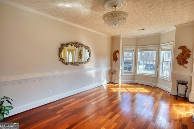 empty room with baseboards, visible vents, ornamental molding, and wood finished floors