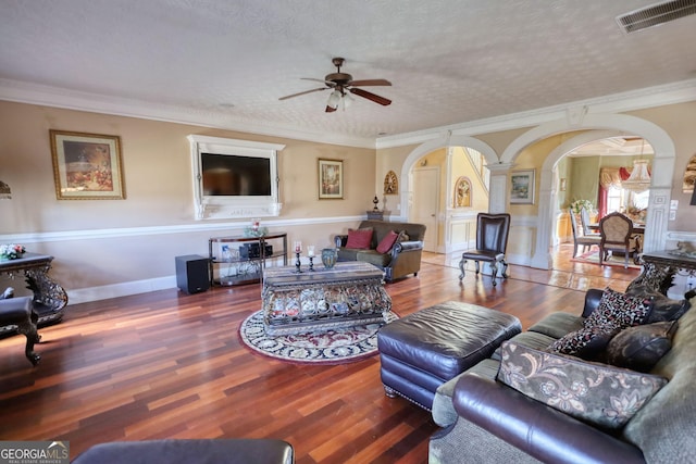 living area featuring arched walkways, a textured ceiling, wood finished floors, visible vents, and crown molding