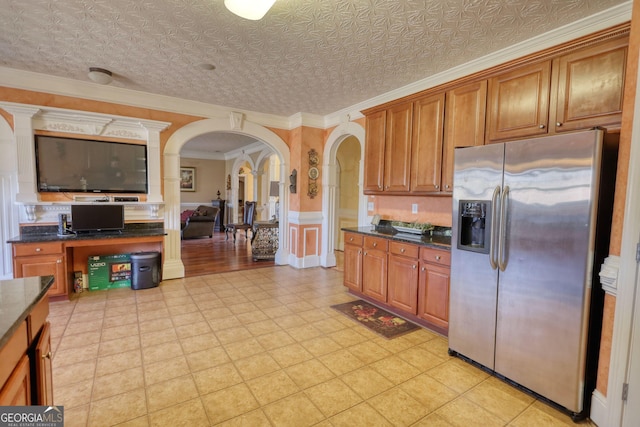 kitchen featuring arched walkways, dark countertops, brown cabinets, and stainless steel refrigerator with ice dispenser