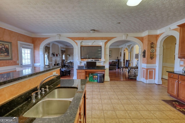 kitchen featuring arched walkways, a sink, ornamental molding, brown cabinets, and dark stone counters