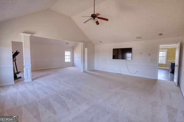 unfurnished living room featuring light carpet, visible vents, a ceiling fan, ornate columns, and high vaulted ceiling