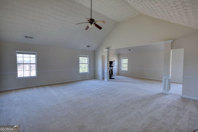 unfurnished living room with high vaulted ceiling, light colored carpet, visible vents, and ornate columns