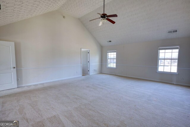 empty room featuring baseboards, high vaulted ceiling, visible vents, and light colored carpet