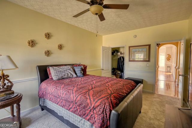 bedroom with a textured ceiling, arched walkways, light carpet, a spacious closet, and a closet