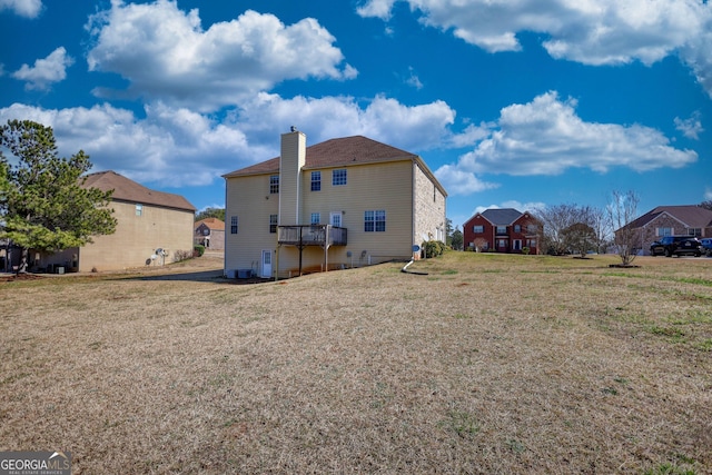 back of house with a deck, a residential view, a lawn, and a chimney