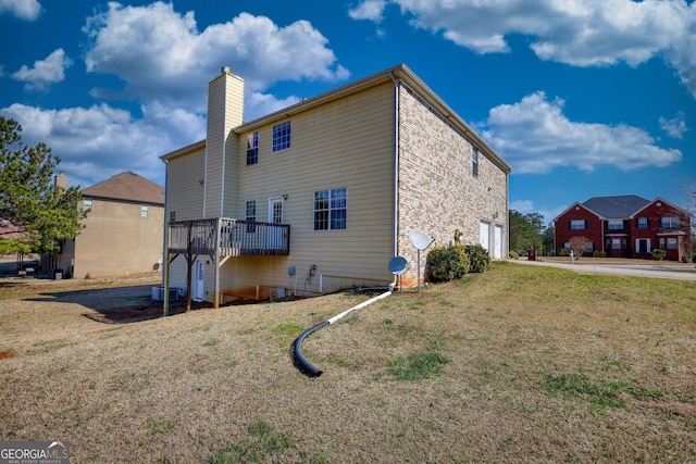 back of property featuring a garage, a yard, concrete driveway, a wooden deck, and a chimney