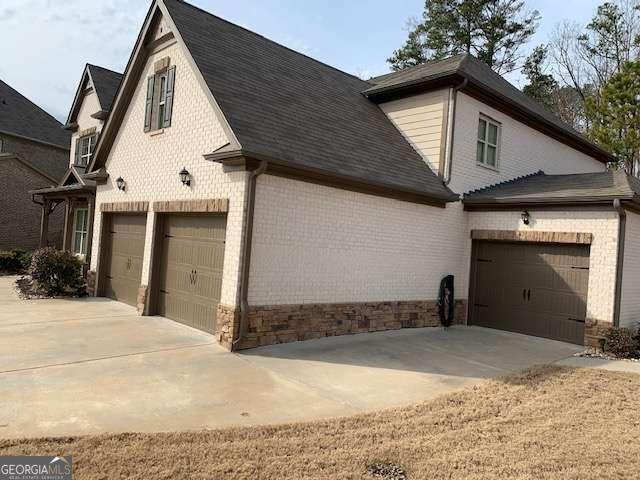 view of side of home featuring driveway, brick siding, and a shingled roof