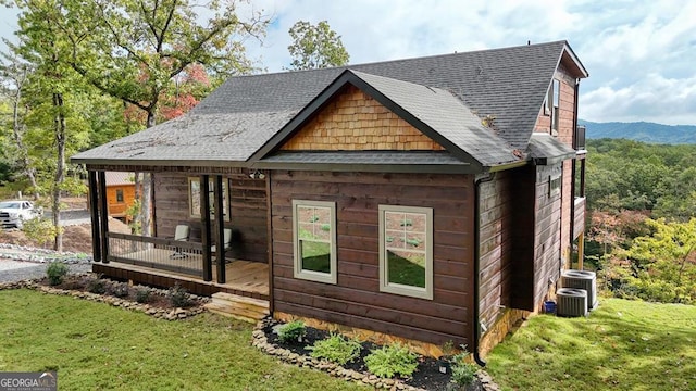 back of house with a shingled roof, a yard, central AC unit, and a mountain view