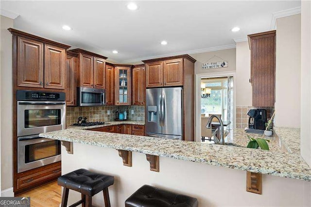 kitchen featuring a kitchen breakfast bar, a peninsula, light stone countertops, stainless steel appliances, and backsplash