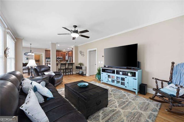 living area featuring light wood-type flooring, baseboards, a ceiling fan, and crown molding