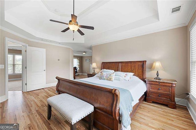 bedroom with light wood-type flooring, a tray ceiling, visible vents, and crown molding