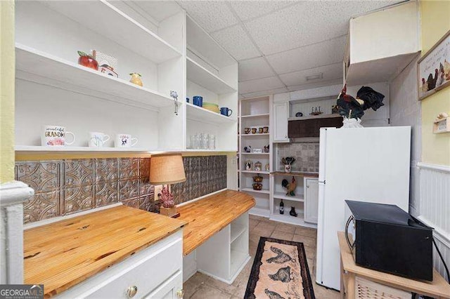 interior space with wood counters, freestanding refrigerator, a paneled ceiling, open shelves, and light tile patterned flooring