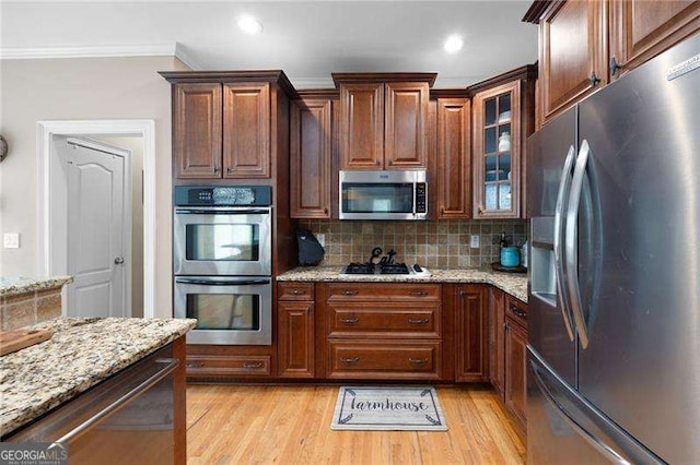 kitchen with light stone counters, light wood-style floors, appliances with stainless steel finishes, tasteful backsplash, and glass insert cabinets