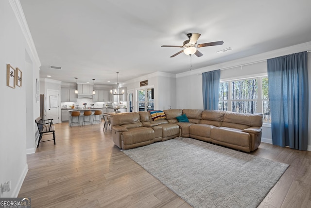 living room featuring ceiling fan with notable chandelier, ornamental molding, visible vents, and light wood-style floors