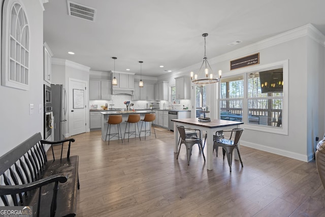 dining area featuring an inviting chandelier, wood finished floors, visible vents, and crown molding