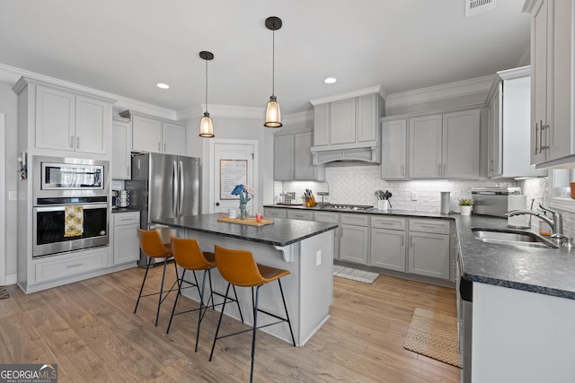 kitchen with dark countertops, a kitchen island, stainless steel appliances, gray cabinetry, and a sink