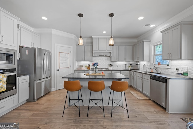 kitchen featuring a center island, pendant lighting, dark countertops, appliances with stainless steel finishes, and a sink